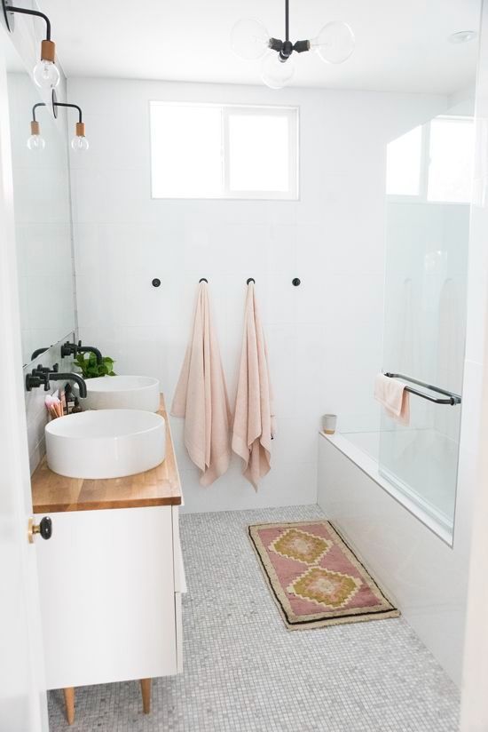 a neutral bathroom clad with different tiles, a white vanity with round sinks, pastel towels and black fixtures is a very chic space