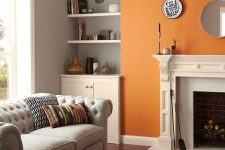 a pretty monochromatic mid-century modern living room done in grey, black and white and cheered up with a bold orange accent wall