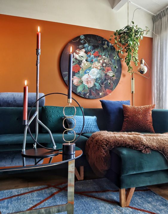 a refined living room with a rust colored accent wall, a teal corner sofa, mismatching pillows, a low coffee table and a bold floral artwork