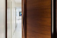 a rich-stained wood clad pivot door with a large and sculptural handle that adds a refined and chic touch to the space