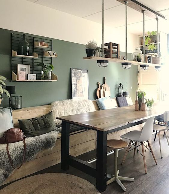 a rustic dining room with a green accent wall, a wooden table and mismatching chairs, a wooden built-in bench with lots of pillows