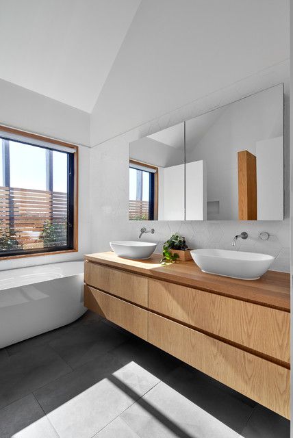a simple contemporary bathroom with a window, a tub, a concrete tile floor, a double light-stained vanity and a mirror storage unit