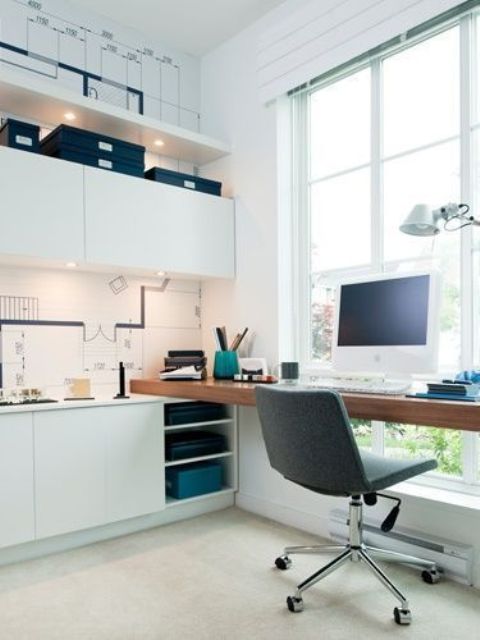 a simple contemporary home office in white, with a floor to ceiling window, sleek cabinets, a floating desk, built-in lights and with a cool view