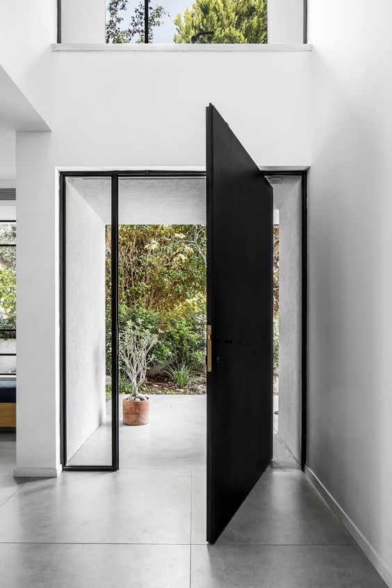 a sleek black pivot door with a delicate gold handle and glass panes is a cool idea for a contemporary or minimalist space