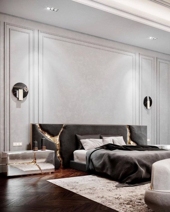 a sophisticated and luxurious contemporary bedroom with neutral paneled walls, a dark upholstered bed, various lamps and cracked touches with gold