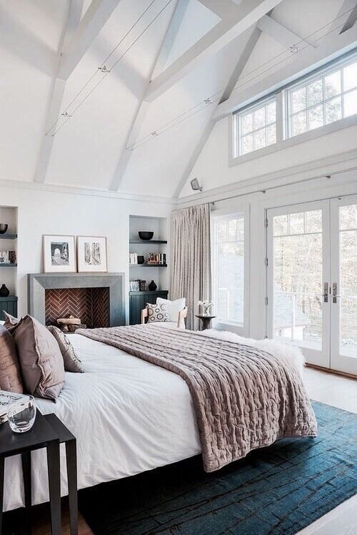 a stylish and welcoming attic bedroom with a fireplace clad with brick, a bed and dark stained nightstands, neutral textiles and a printed rug