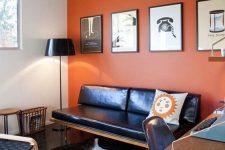 a stylish orange home office with a dark wooden beam, a black leather daybed, black chairs, a cool desk and layered rugs plus a gallery wall