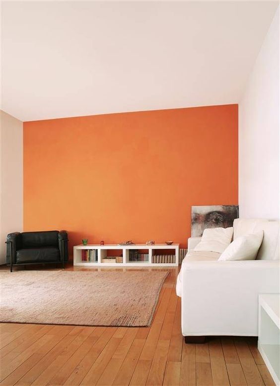 a very laconic living room with an orange accent wall, a white sofa, a sideboard, a black chair and a bold artwork is cool