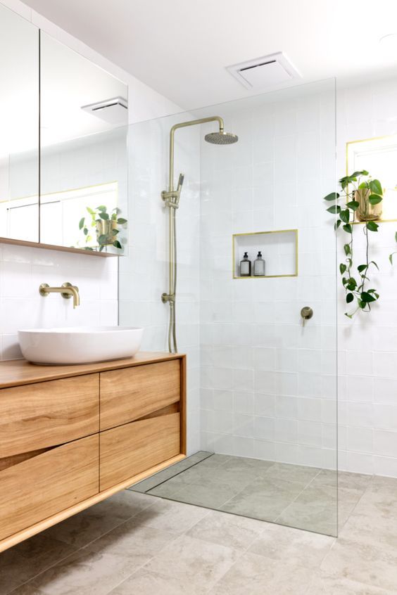 a welcoming and neutral bathroom with white and grey square tiles, a floating sleek vanity, potted greenery and gold fixtures is cool