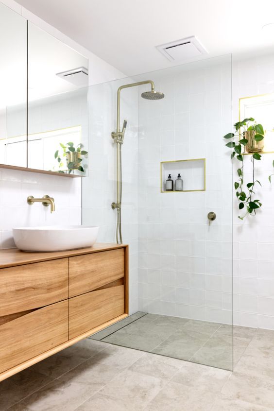 a welcoming and neutral bathroom with white and grey square tiles, a floating sleek vanity, potted greenery and gold fixtures is cool