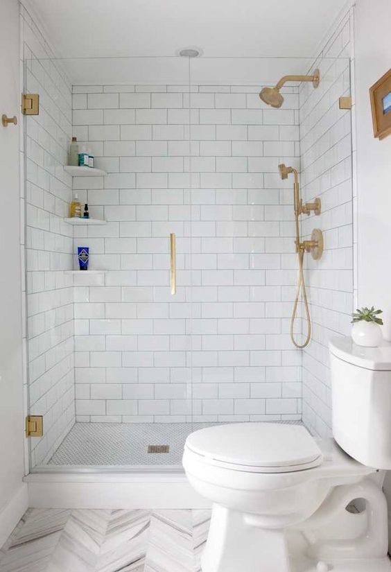 a white bathroom with subway and chevron tiles, gold fixtures and white appliances is a stylish idea that always works