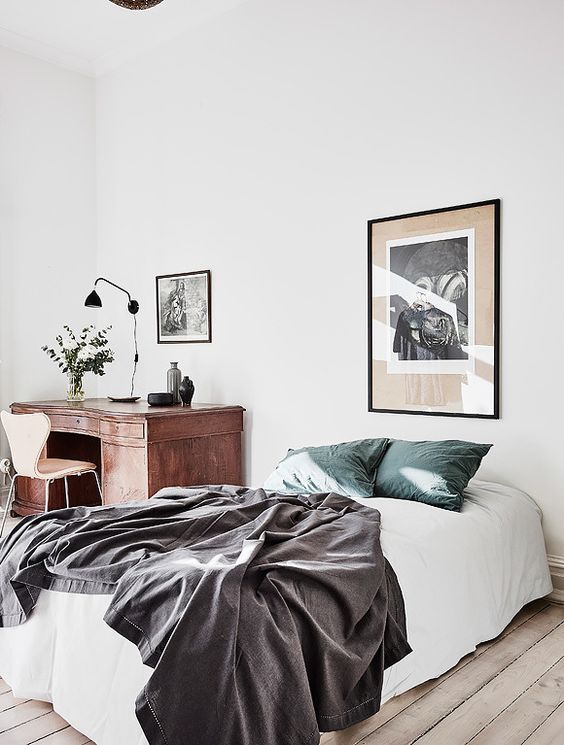 an airy and light bedroom with a bed and a vintage wooden desk in the corner plus some chic artworks is a lovely space