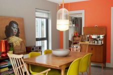 an eclectic dining room with an orange accent wall, a wooden table, neon yellow chairs and wooden ones plus mid-century modern furniture