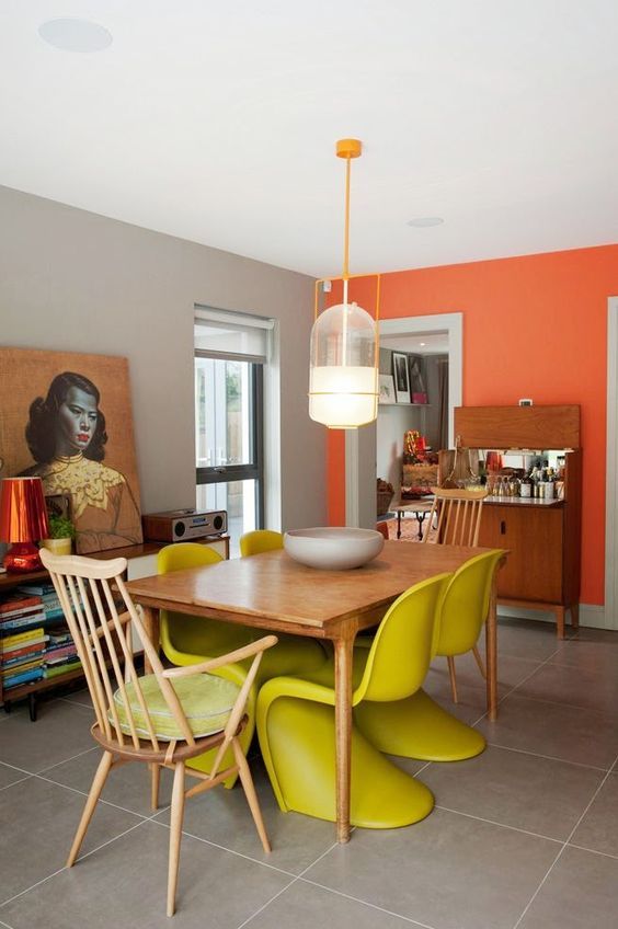 an eclectic dining room with an orange accent wall, a wooden table, neon yellow chairs and wooden ones plus mid century modern furniture