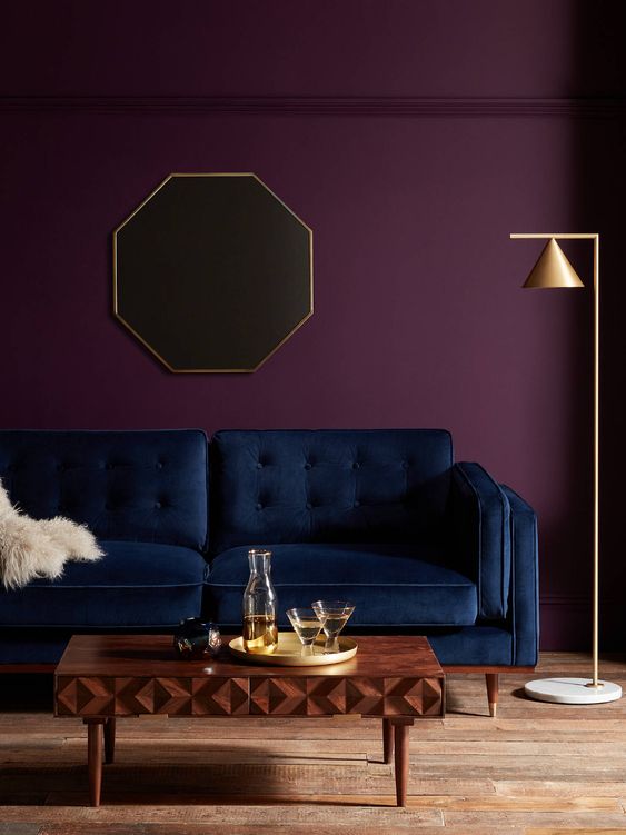 an exquisite living room with a deep purple accent wall, a navy sofa, a beautiful wooden coffee table and a gold floor lamp
