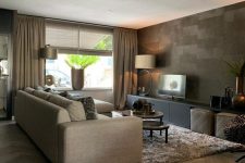 02 a catchy and stylish living room with an accent taupe wall, tan curtains and a sofa, a tan rug, tan leather poufs and a black TV unit