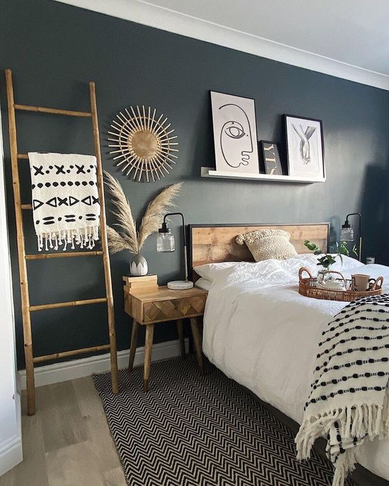 a beautiful black bedroom with a wooden bed, nightstands, a ledge with artworks, a ladder, pampas grass and a bold starburst decoration