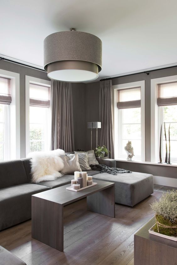 a lovely taupe contemporary living room with a matching low sofa, taupe curtains, a taupe coffee table with lots of candles and a taupe pendant lamp