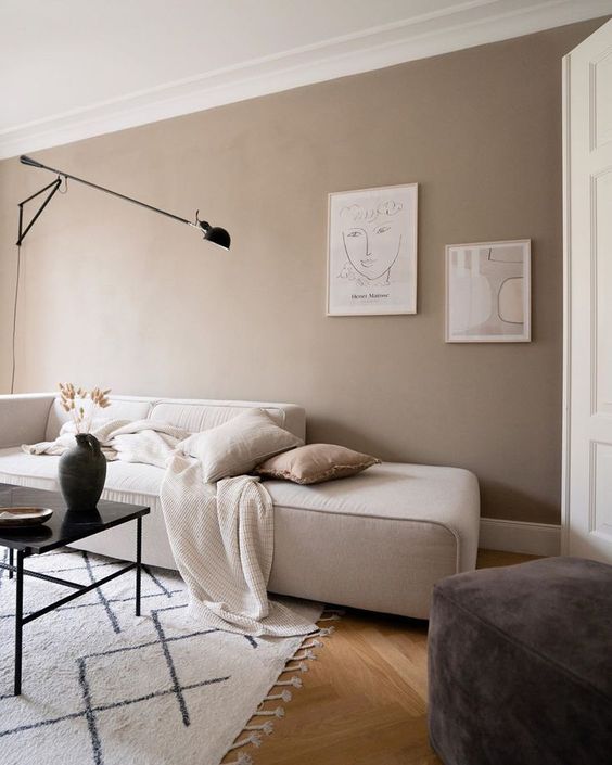 a Scandinavian living room with taupe walls, a creamy low sofa, a black table, a brown pouf and a mini gallery wall