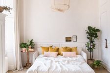 10 a pretty light-filled bedroom with paneled walls, a white bed, a pendant lamp, mustard and pink pillows and some potted greenery to refresh the space
