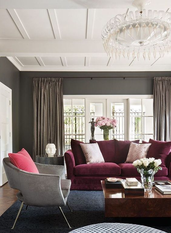 a taupe living room with brown curtains, a grey chair, a purple sofa, a stone slab coffee table and a beautiful crystal chandelier