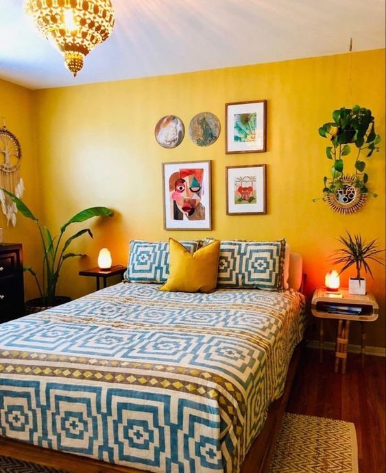 a bold bedroom with yellow walls, geometric bedding and a yellow pillow, mismatching nightstands, a colorful gallery wall and potted plants