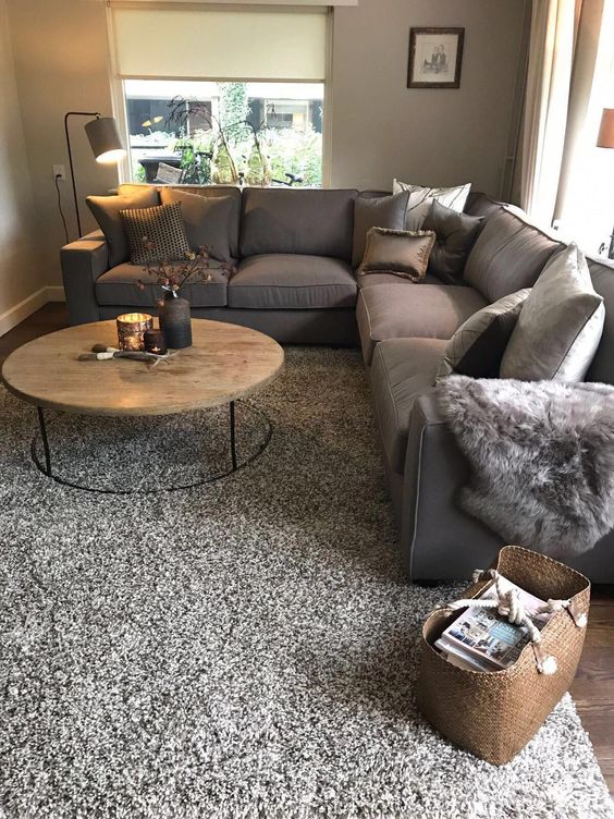 a grey living room with a large taupe sectional, a round coffee table, a floor lamp, various pillows and a taupe rug