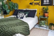 22 a pretty bedroom spruced up with Gen Z yellow – an accent wall, a bed with black, green and neutral bedding, potted plants, artworks and a green table is super cool