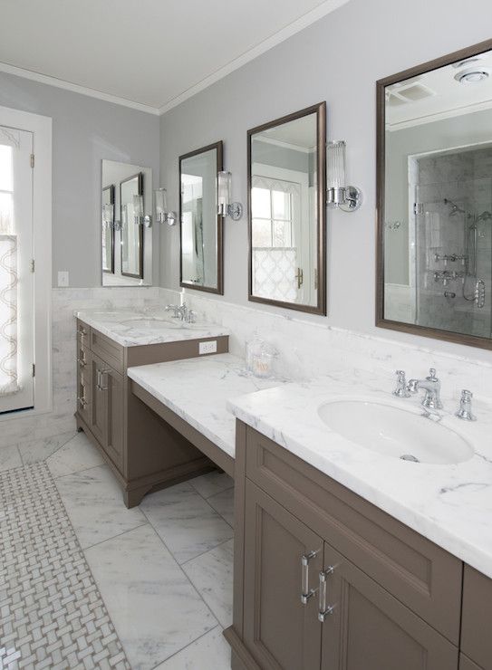 a beautiful bathroom clad with white stone tiles, a large taupe double vanity, mirrors in brown frames, sconces and vintage fixtures
