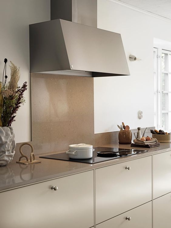 a beautiful modern gray kitchen with a taupe stone backsplash and countertops, a matching hood, brass knows and some dried grasses is very chic