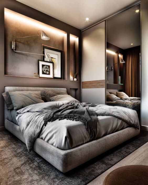a beautiful taupe bedroom with lit up niches, a floating upholstered bed, grey bedding, lamps and a storage unit with a mirror sliding door