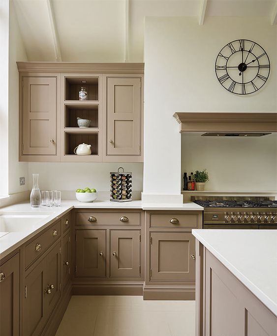 a beautiful taupe vintage kitchen with shaker cabinets, white countertops and a backsplash, a cooker with a hood, a catchy clock and vintage knobs