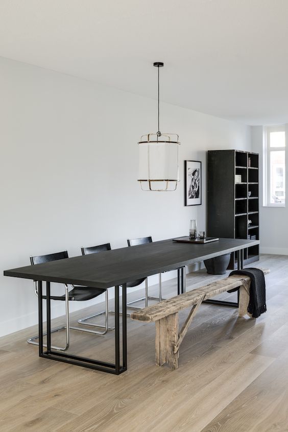 a catchy contemporary dining room with a black table, black leather chairs, a rustic wooden bench and a pendant lam[