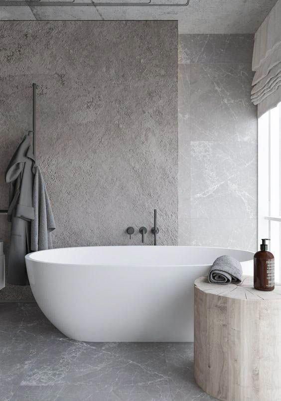 a chic bathroom done with grey marble, with a textural taupe stone accent wall, an oval tub, a tree stump as a side table and neutral textiles