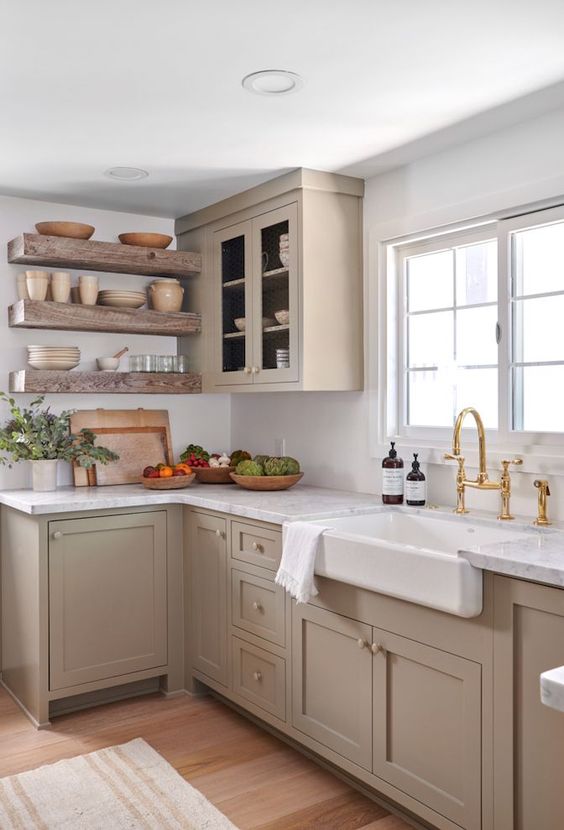 a chic taupe farmhouse kitchen with shaker cabinets, open shelves, white stone countertops and a backsplash and gold fixtures is amazing