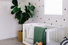 a contemporary nursery with a geo printed accent wall, a white crib, a grey chair, a potted plant, a color block basket