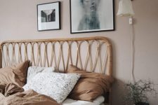 a cozy bedroom with light taupe walls, a rattan bed and a stool, a mini gallery wall and a potted plant plus sconces