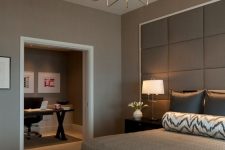 a lovely modern bedroom with taupe walls, a bed with an oversized upholstered headboard, an upholstered bench and a lovely chandelier