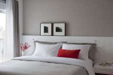 a lovely small bedroom with a taupe accent wall, a bed with an extended white headboard, floating nightstands and touches of red