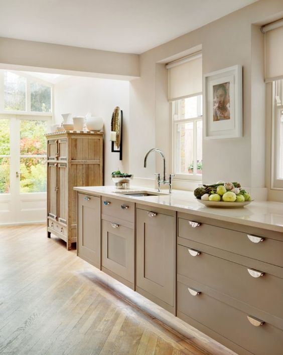 a lovely taupe kitchen with shaker cabinets, vintage knobs, white stone countertops and a vintage rustic cupboard for storage