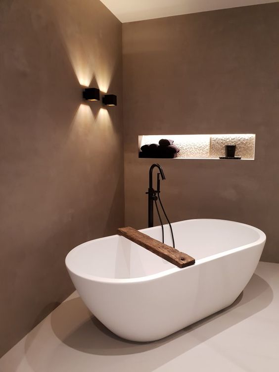 a minimalist taupe bathroom with a chic oval tub, a niche for storage and black fixtures for a more modern feel is a lovely space