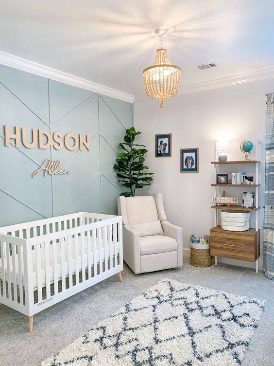 a modern nursery with a green paneled accent wall, a white crib and chair, a shelf unit with a cabinet, a potted plant and a pendant lamp