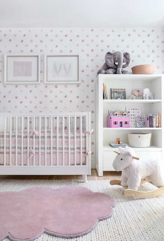 a pretty contemporary nursery with a pink spot accent wall, a white crib and a storage unit, layered rugs, pink bedding and lovely toys