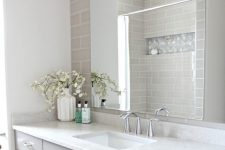 a refined bathroom with skinny taupe tiles, a taupe vanity, a white countertop, an oversized mirror and a large sconce is a pretty idea