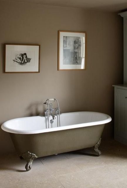 a refined bathroom with taupe walls, a tan floor, a taupe clawfoot tub, a white storage unit and a mini gallery wall is all chic