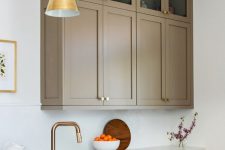 a refined taupe kitchen with shaker cabinets – mostly lower and a couple of upper ones, white stone countertops and a backsplash, gold pendant lamps