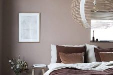 a relaxed bedroom with a taupe accent wall, a wooden bed and stools, an oversized wooden lampshade and some art