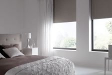 a small white bedroom with a tan upholstered bed, taupe bedding and matching sleek shades and a chair is a very chic idea