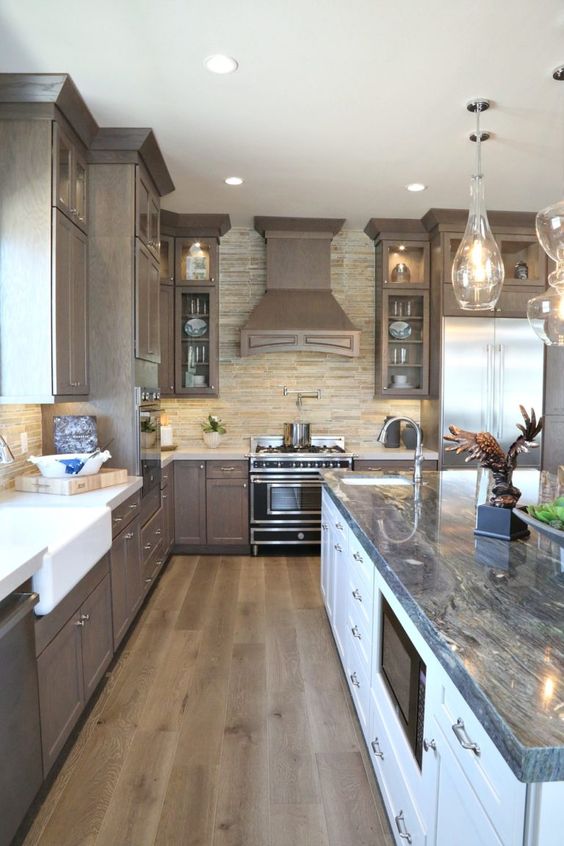 a vintage taupe kitchen wiht shaker cabinets, a grey stone tile backasplash and white cputnertops, a large kitchen island with a stone coutnertop and pendant lamps
