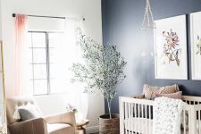 a welcoming boho nursery with a navy accent wall, a white crib and a tan rocker chair, layered rugs, a pendant lamp and some knit pieces